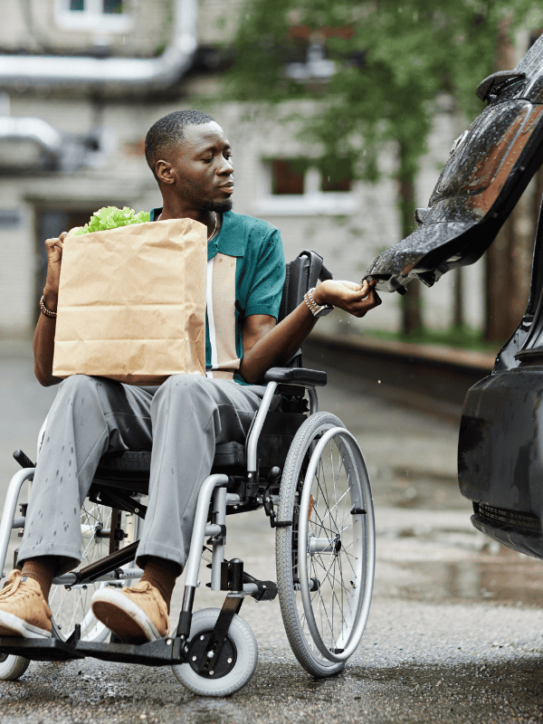 black man lifting lid to suv for bag of groceries in a wheelchair in the rain